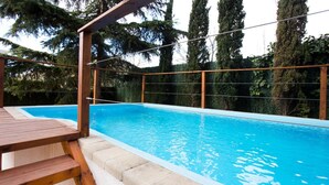A swimming pool with a wooden deck and a metal fence, surrounded by tall trees.