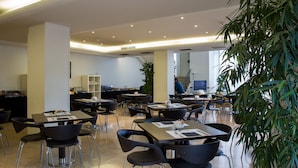 A modern dining area with multiple tables and chairs, a staircase in the background, and a large potted plant.