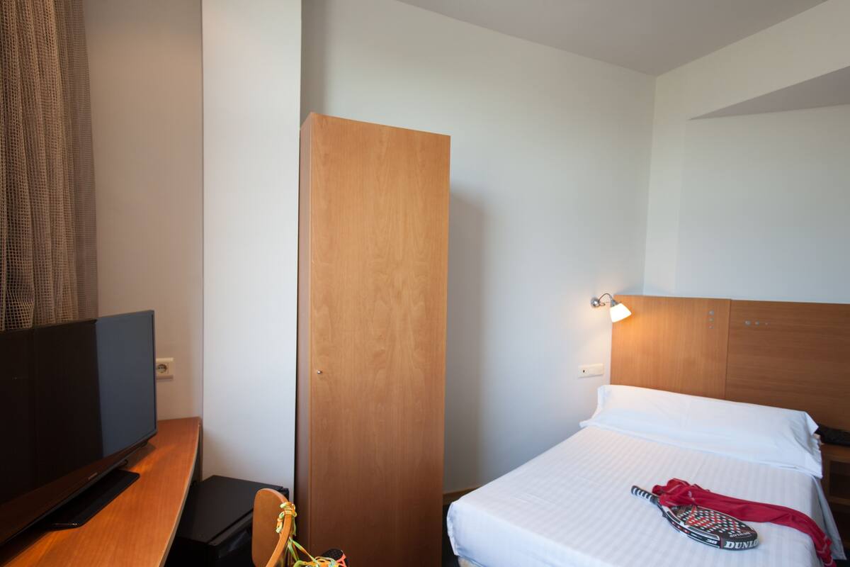Una habitación de hotel con cama, televisión, armario de madera y lámpara.