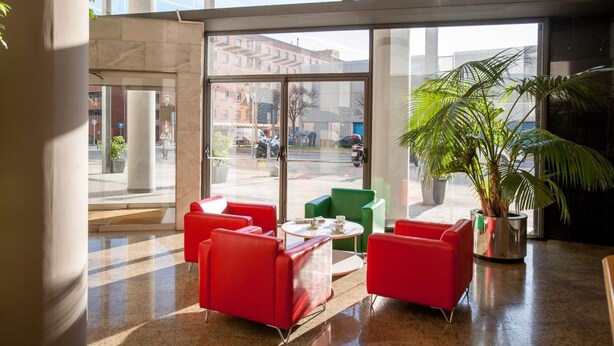 A lobby with large windows, red and green seating, and a potted plant.
