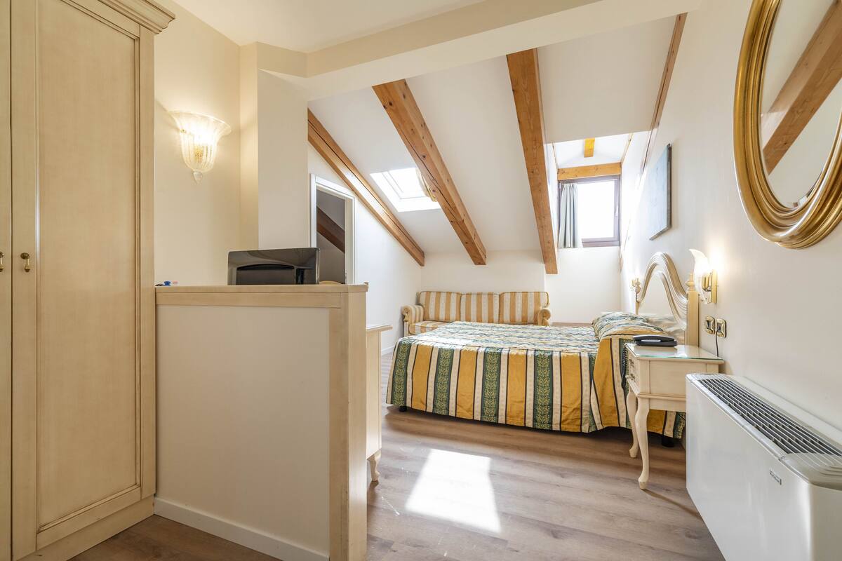 A bedroom with a bed, bedside table, and a heater. There is a wardrobe and a window with a view.