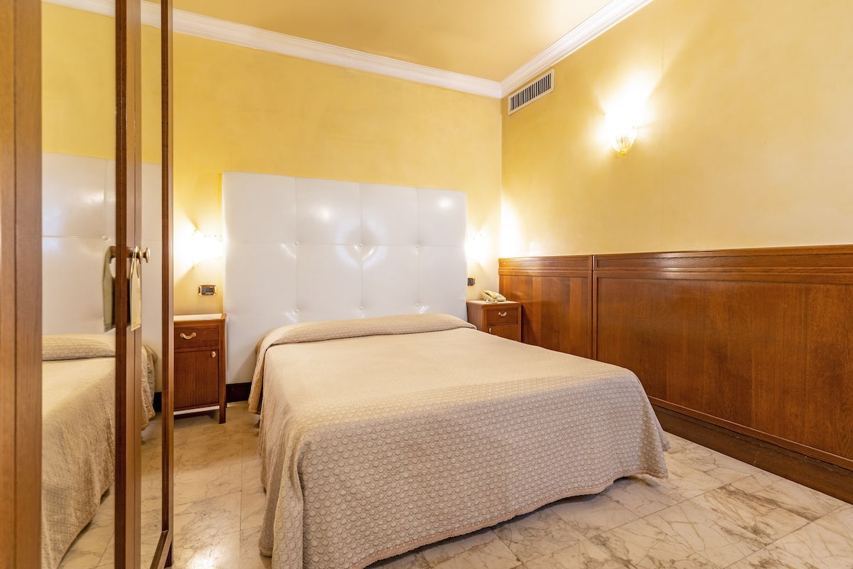 A hotel room with a large bed, bedside tables, and a wooden headboard.