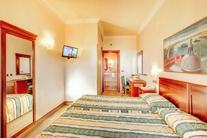 Hotellihuone, jossa on suuri sänky, työpöytä, tuoli, televisio ja taulu seinällä.