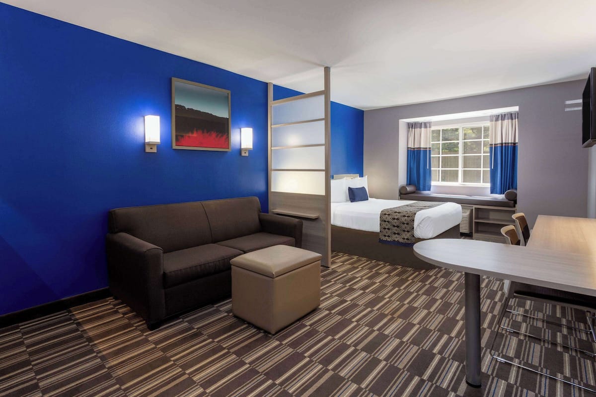 A hotel room with a blue wall, a sofa, a small table, a bed, and a window with curtains.