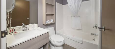 A modern bathroom with a white sink, vanity, and toilet. It includes a shower with a curtain and a bathtub.