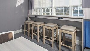 Una habitación con una mesa de comedor, cuatro taburetes de madera, una ventana con persianas y vista al exterior.
