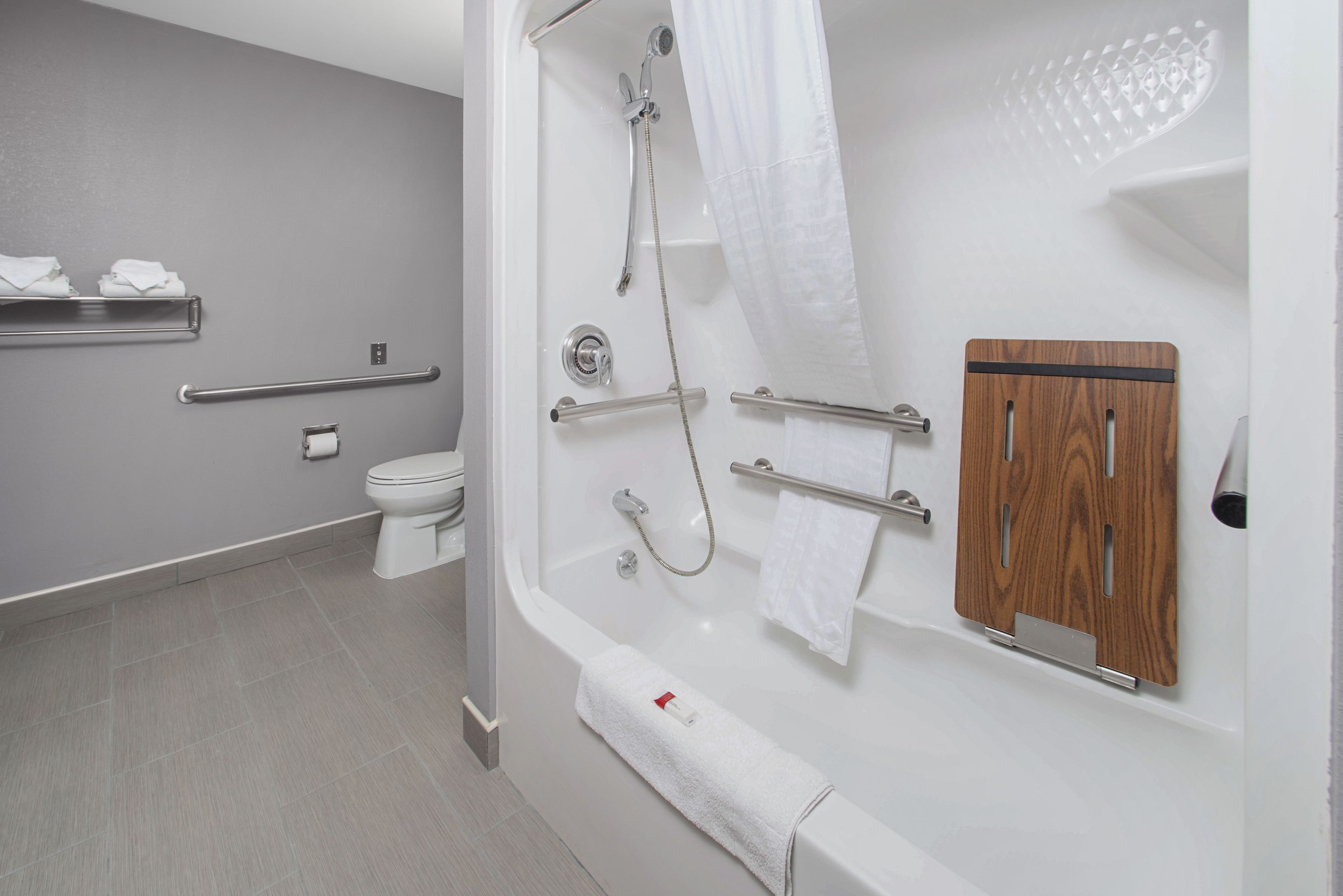 Un baño moderno con bañera, ducha, inodoro y barras de apoyo.