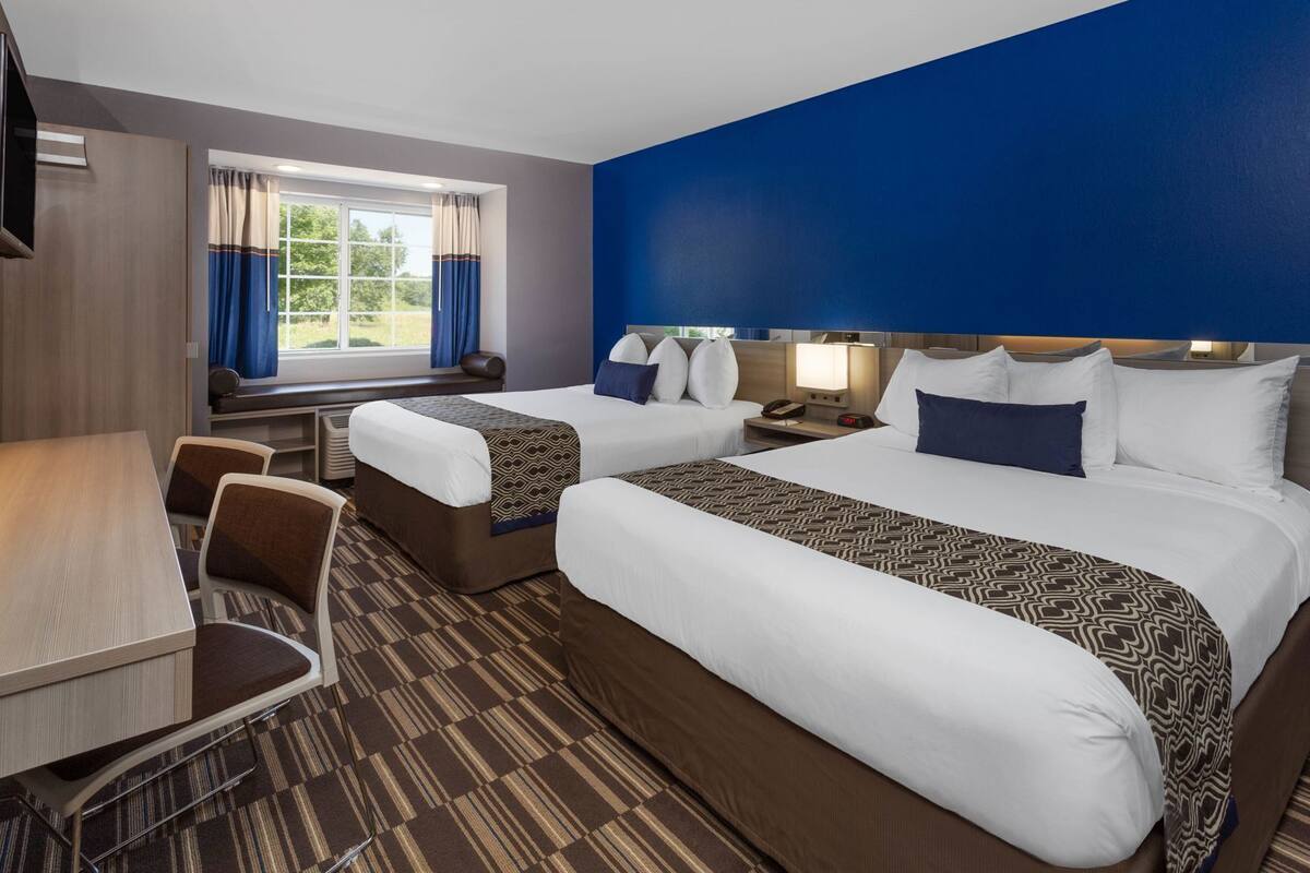 A hotel room with two beds, a desk, and a chair.
