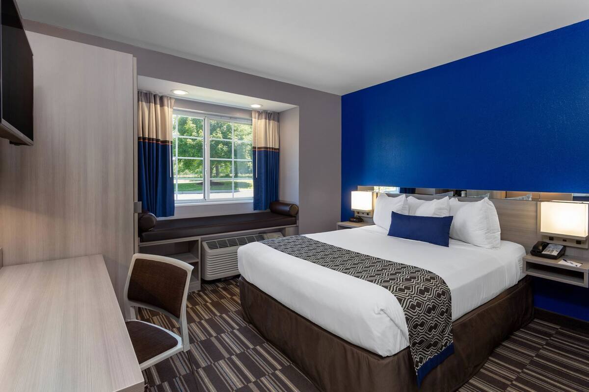 A hotel room with a bed, desk, chair, and a window with curtains.