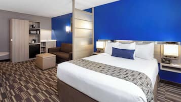 A hotel room with a large bed, a desk with a computer, a chair, a small kitchenette, and a bathroom.