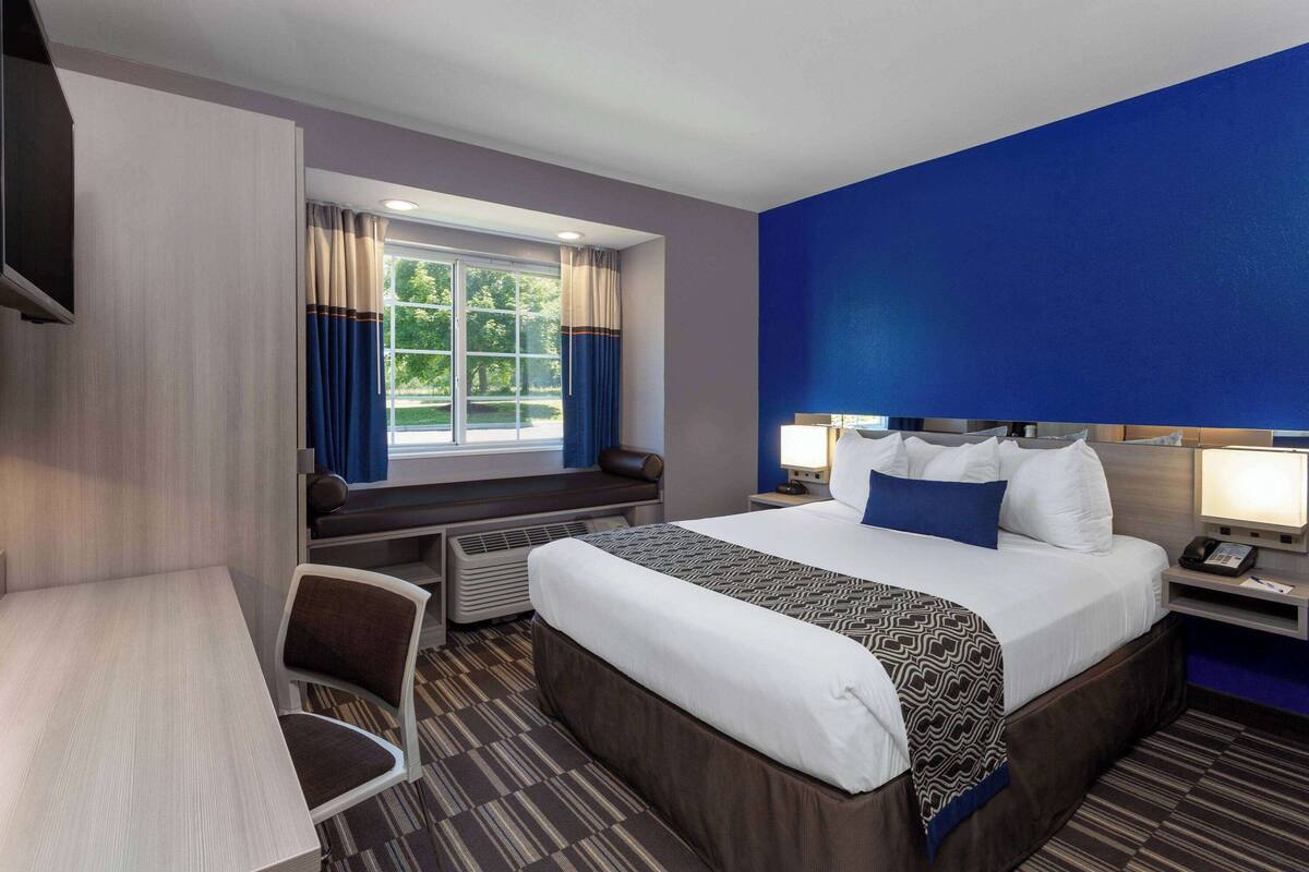 A hotel room with a bed, bedside table, lamp, and a window with curtains.