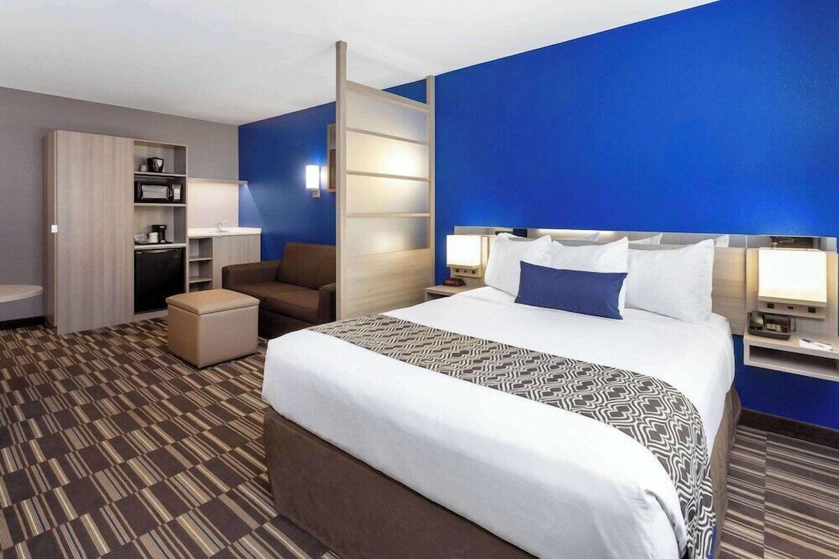 A hotel room with a large bed, a desk with a computer, a chair, a small table, and a sofa.