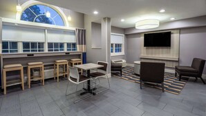 Una habitación de hotel moderna con comedor, televisión y un amplio ventanal con cortinas.