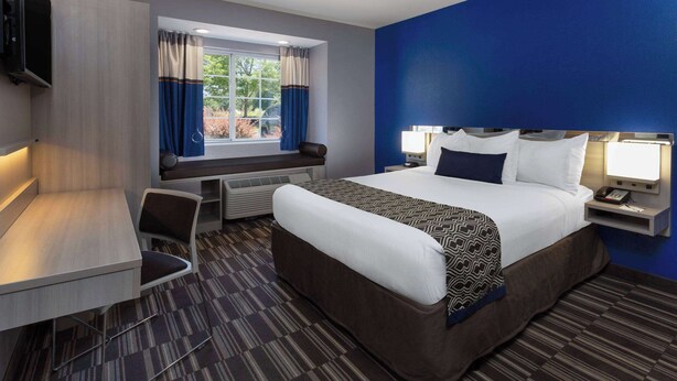 Habitación de hotel con cama, escritorio, silla, televisión y ventana con cortinas.