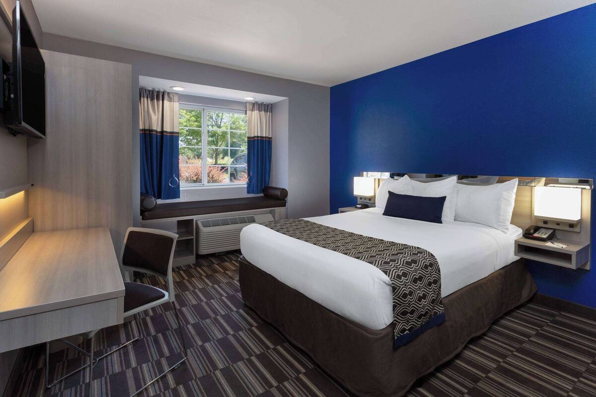 A hotel room with a bed, a desk, a chair, a TV, and a window with curtains.