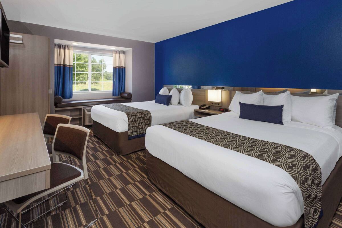 A hotel room with two beds, a desk, and a chair.