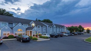 Un hotel con una fila de coches aparcados frente a él, una zona de aparcamiento cubierta y un cielo al atardecer.