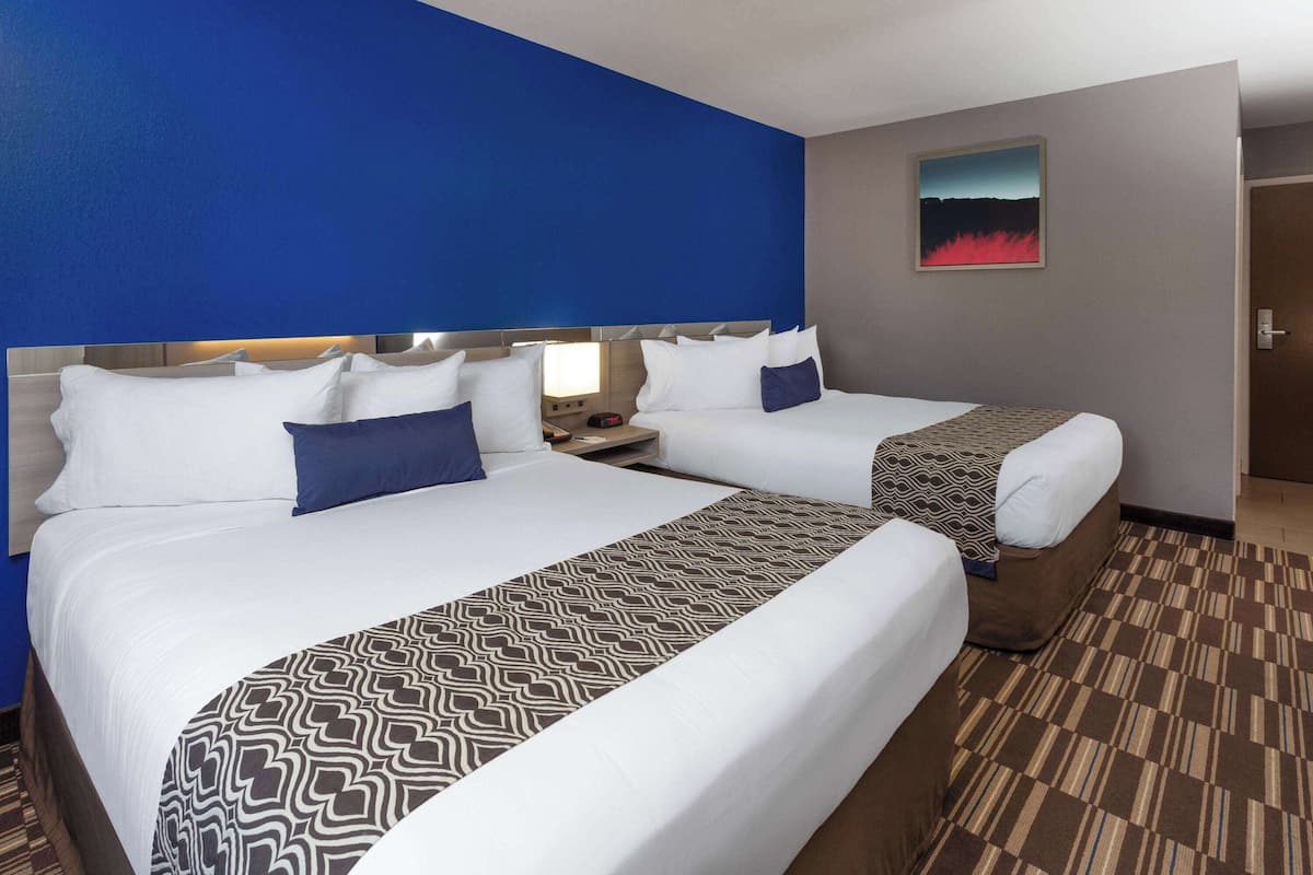 A hotel room with two beds, a patterned bedspread, and a painting on the wall.