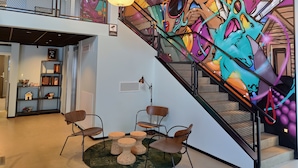 Een modern interieur met een levendige graffiti muurschildering, een trap met een gaasleunbaan, en een zithoek met stoelen en een kleine tafel.