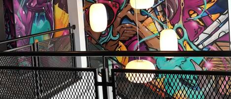 A modern interior with a vibrant graffiti mural, hanging pendant lights, and a metal railing.