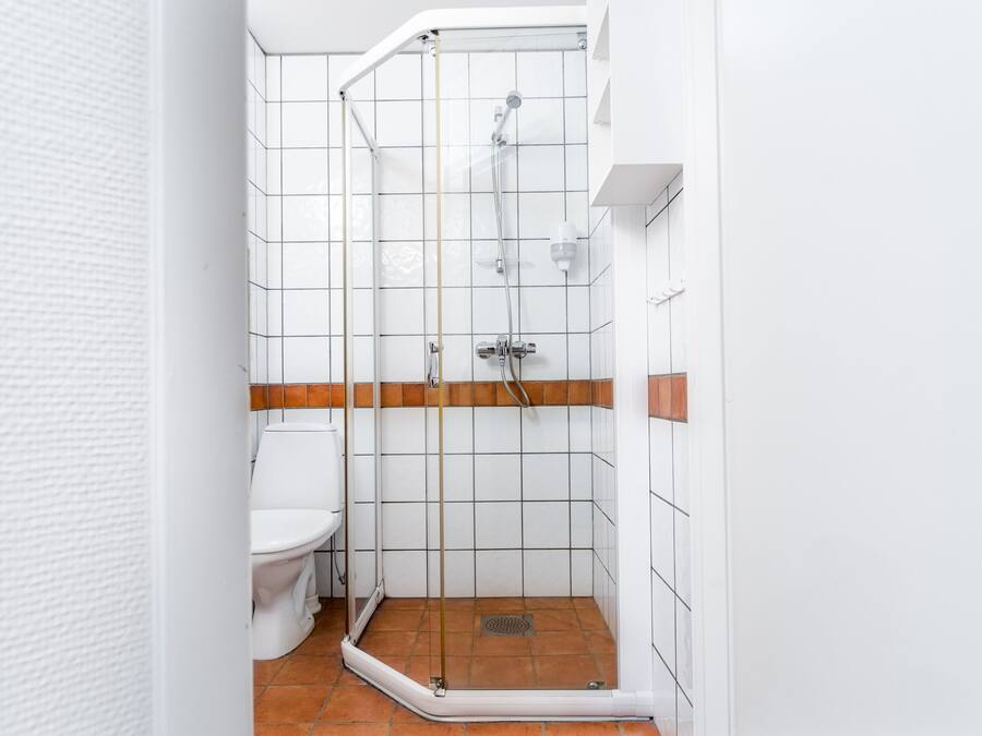 Un baño con inodoro blanco, cabina de ducha de vidrio y suelo de ducha con azulejos marrones.