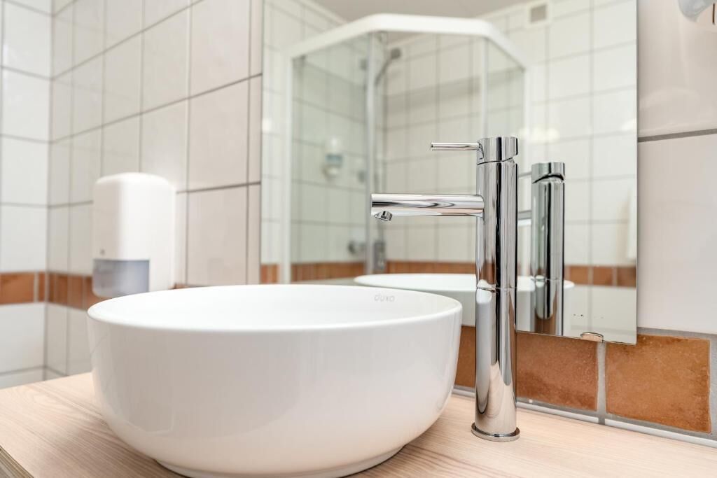 Un baño moderno con un lavamanos de cerámica blanca, grifos cromados y un box de ducha de vidrio.