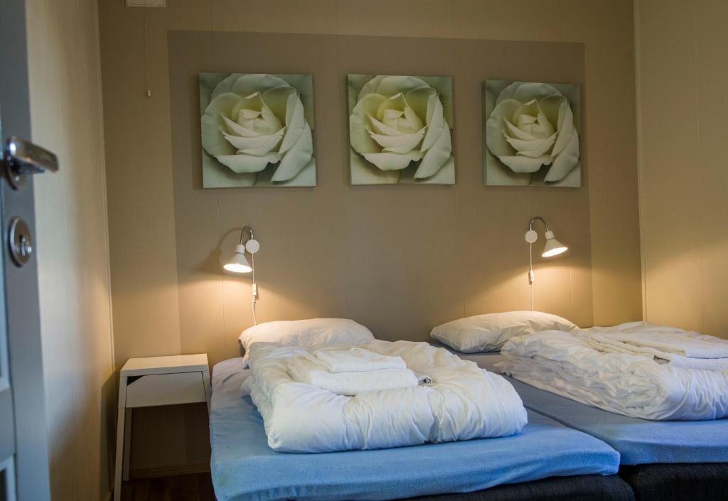 Habitación de hotel con dos camas, una mesita de noche y lámparas fijadas a la pared.