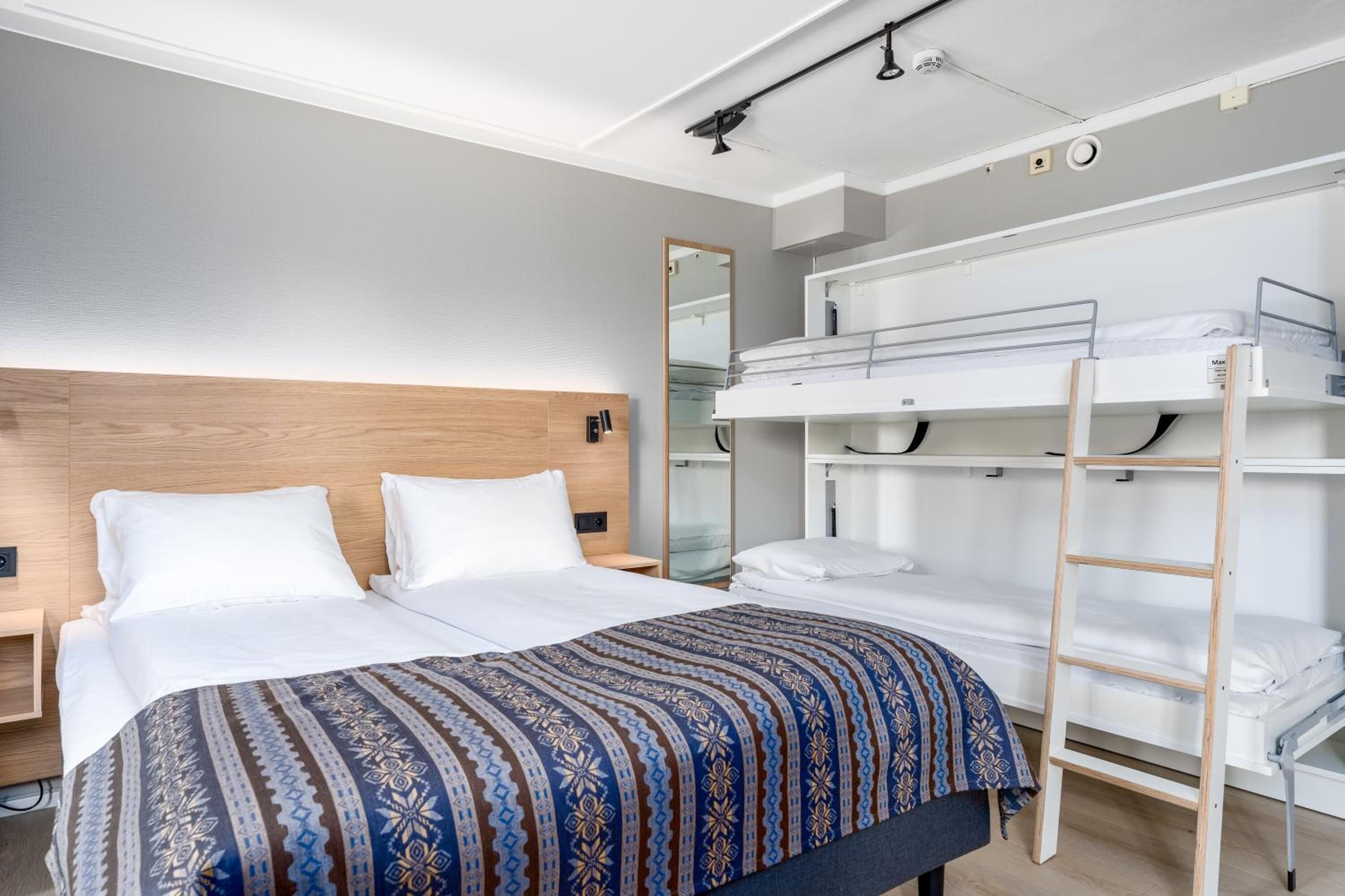 Ein modernes Hotelzimmer mit einem großen Bett, einem Stockbett und einer Leiter.