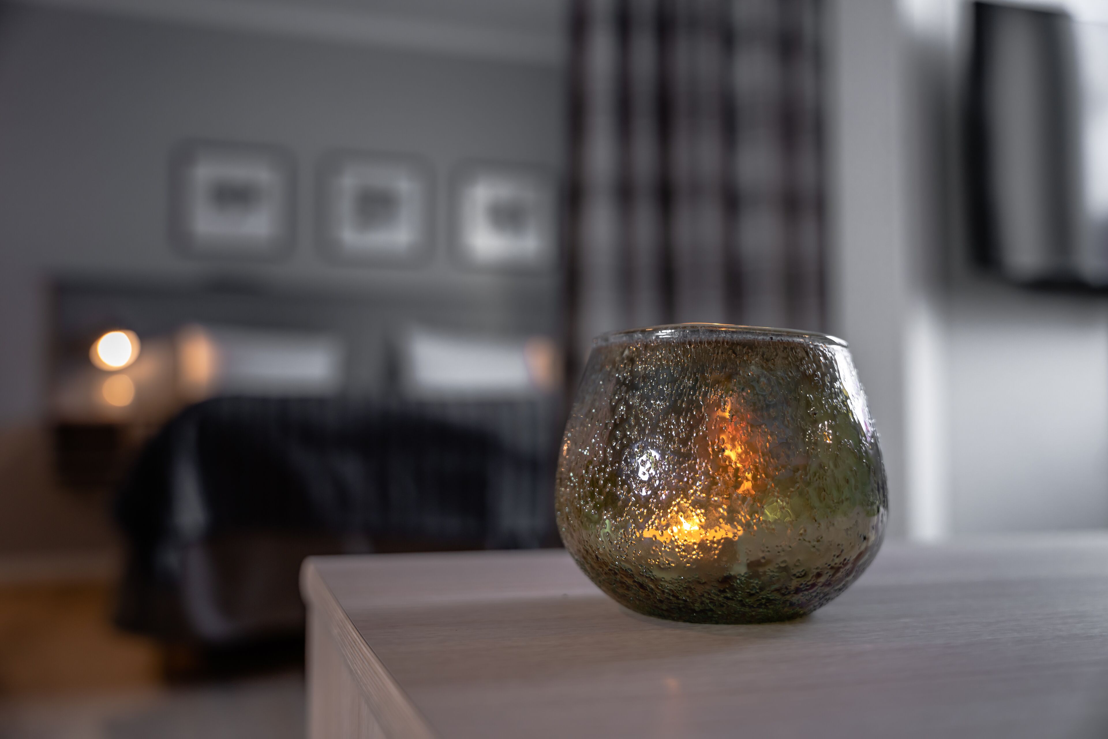 A candle on a table in a room with a bed and a wall-mounted TV.