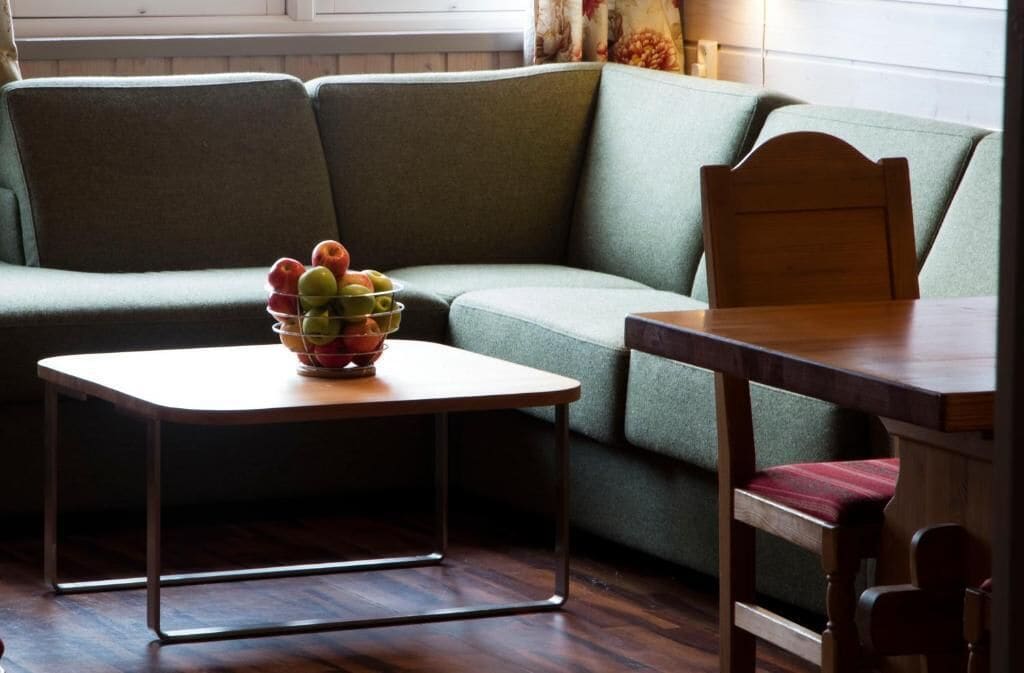 A room with a green sofa, a wooden table, and a bowl of fruit.