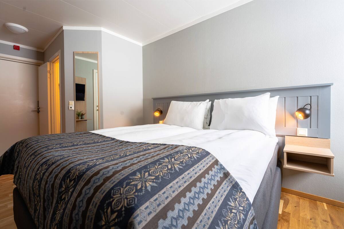 A neatly made bed with a patterned blanket, a bedside table with a lamp, and a mirror on the wall.