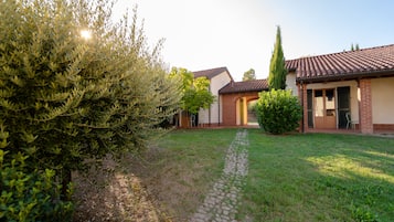 Una casa con camino de entrada pavimentado que conduce a una puerta principal, rodeada de follaje y un cielo despejado.