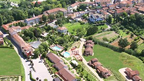 Vista aérea de una zona residencial con piscina, un edificio grande con techo rojo y vegetación circundante.