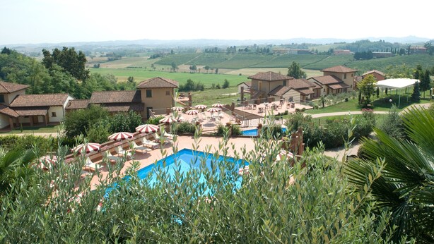 Un resort con piscina rodeada de tumbonas y sombrillas, con colinas ondulantes y un cielo despejado al fondo.