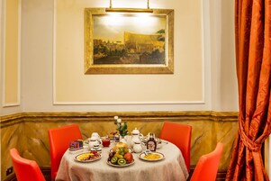 A dining table with a variety of dishes, a painting on the wall, and orange chairs.