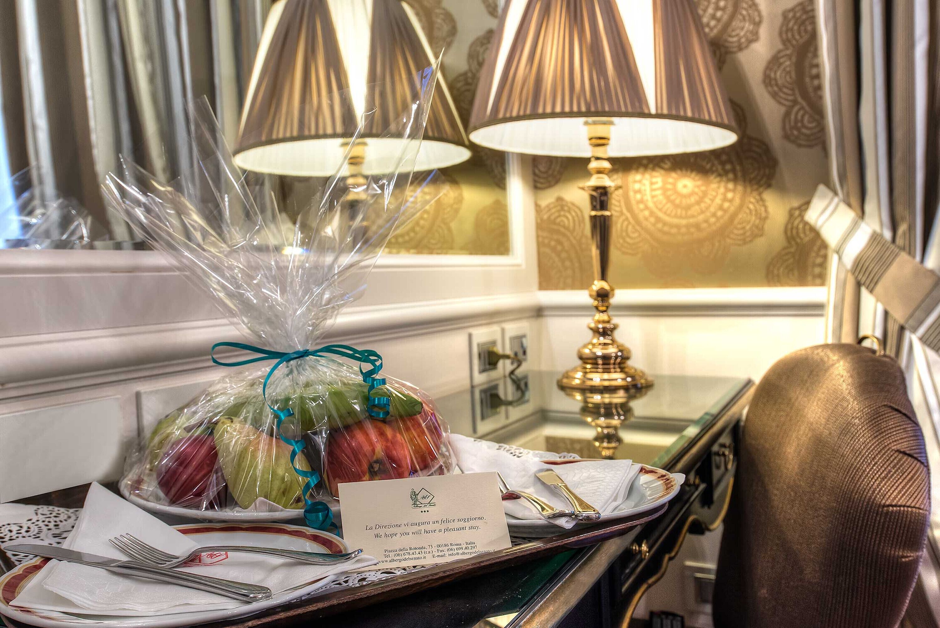 Ein Hotelzimmer mit einem Esstisch, gedeckt mit Tellern, Besteck und einem Obstkorb. Eine Lampe und ein Sessel sind ebenfalls zu sehen.