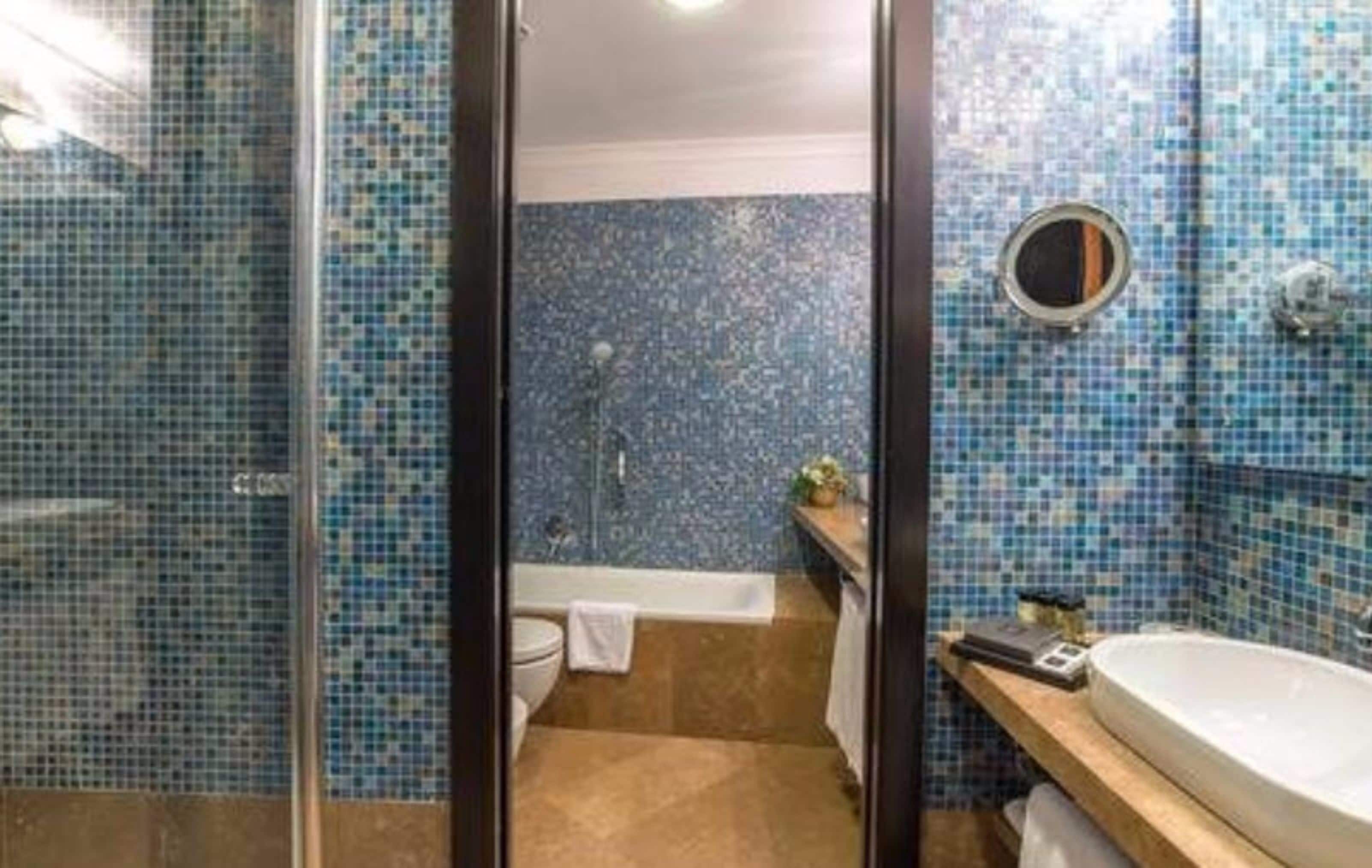 Et badeværelse med mosaikflisevægge, et badekar, et toilet og en håndvask.
