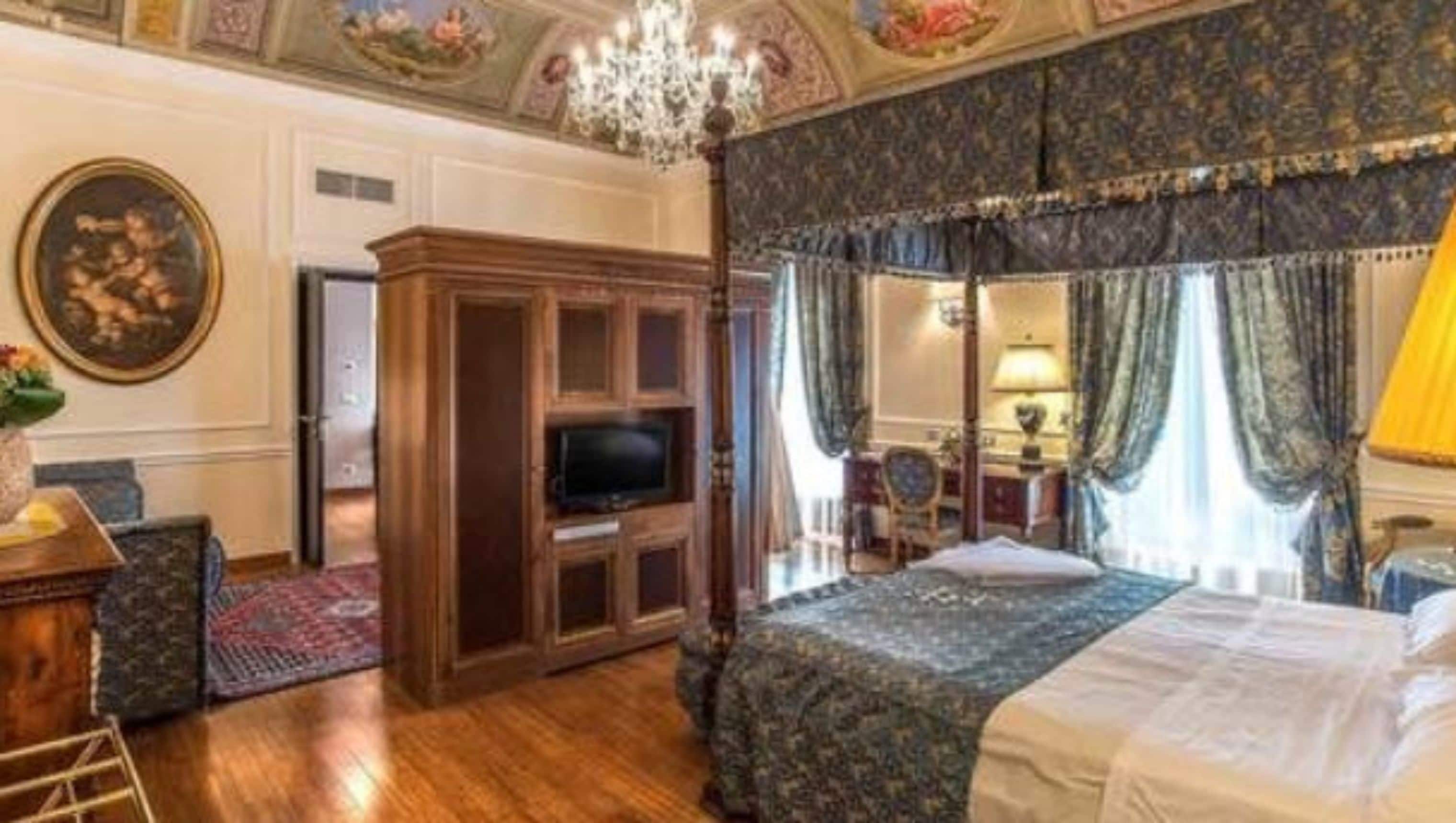 A traditional four-poster bed with a canopy, a wooden cabinet with a television, and a chandelier.