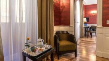 Ein Hotelzimmer mit Holzboden, einem Esstisch mit einem Tablett mit Frühstücksangeboten, einem Stuhl und Blick auf den Speisesaal.
