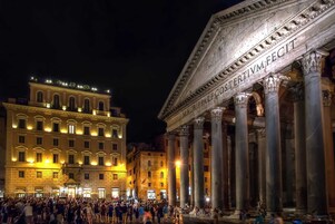 A historic building with classical architecture, including columns and inscriptions, and a crowd of people in front.