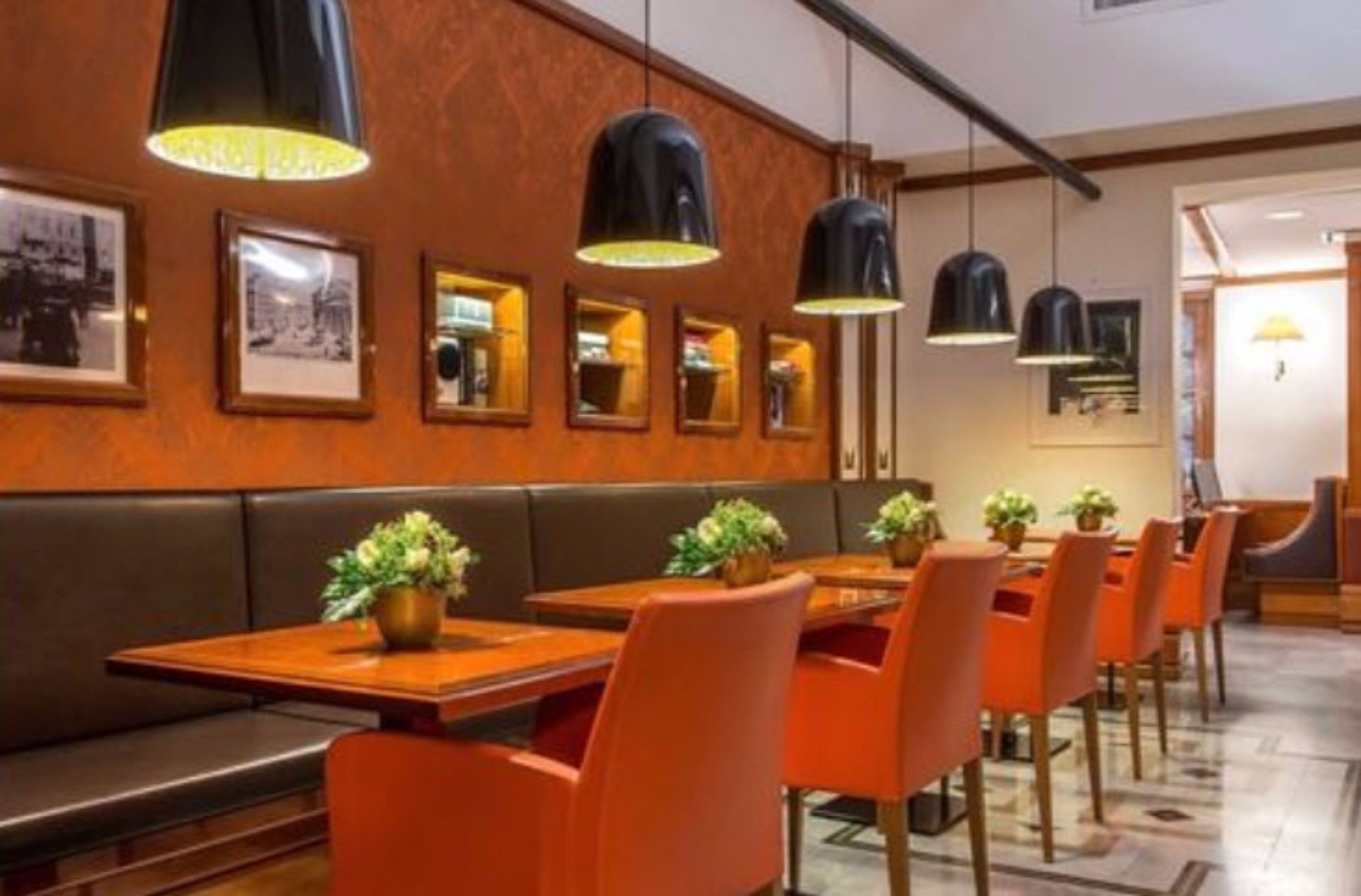 A restaurant with wooden tables and orange chairs, black pendant lights, and framed pictures on the wall.