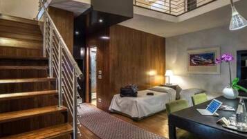 Una habitación de hotel moderna con una escalera de madera, una cama con cubrecama blanco, un escritorio con una computadora portátil y un florero con flores.