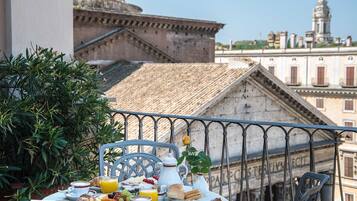 Una mesa en el balcón con cosas para el desayuno, una planta en maceta y vistas a edificios históricos.
