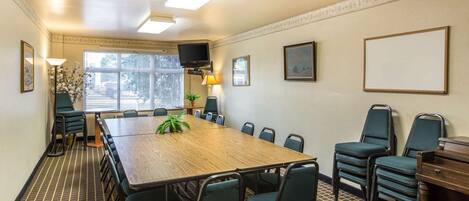 A conference room with a large wooden table, green chairs, a TV, and framed pictures on the walls.