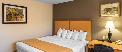 Habitación de hotel con cama, escritorio, silla, lámpara y dos cuadros en las paredes.
