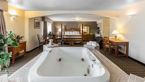 Habitación de hotel con una bañera grande, una cama con cabecera de madera, un escritorio con lámpara y una silla.