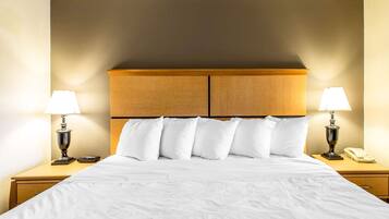 Una habitación de hotel con una cama grande, dos mesitas de noche, un cabecero de madera y dos lámparas.