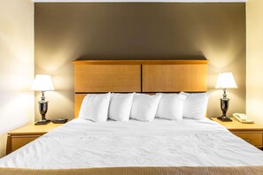 A hotel room with a large bed, two bedside tables, a wooden headboard, and two lamps.