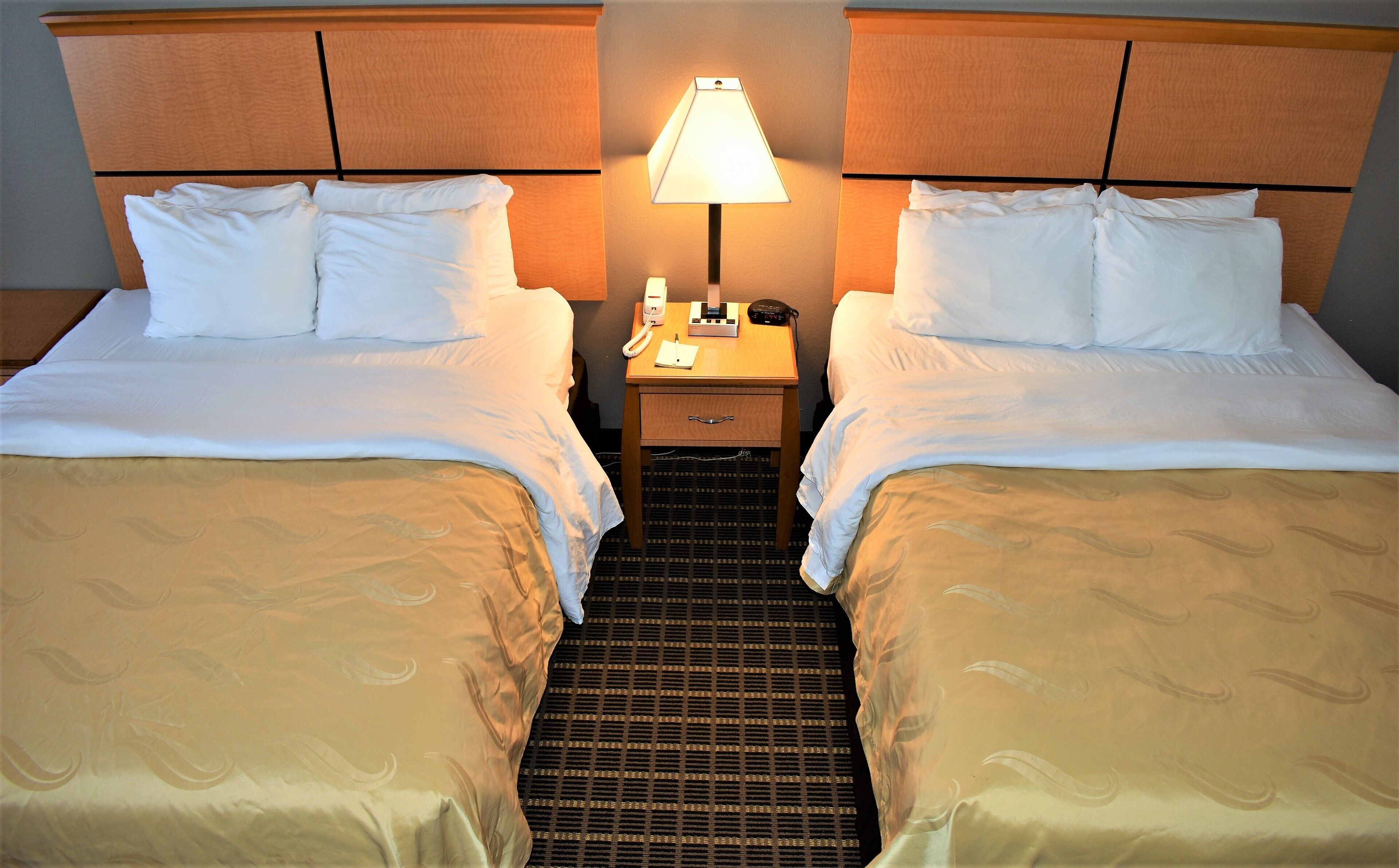 A hotel room with two beds, a nightstand with a lamp, and a small drawer.
