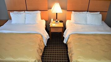 A hotel room with two beds, a nightstand with a lamp, and a small drawer.